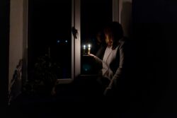 Frau steht mit einer Kerze bei einem Blackout in der dunklen Wohnung am Fenster
